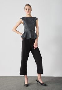 Čierny peplum top s šedými vertikálnymi pruhmi, opásaný v páse; v kombinácii s čiernymi širokými nohavicami a čiernymi vysokými podpätkami.