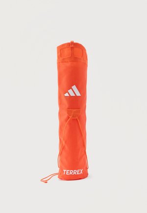 Jasnopomarańczowa, cylindryczna torba na ramię z logo Adidas i napisem "TERREX", wyposażona w ściągacz na sznurek i pętlę do trzymania u góry.