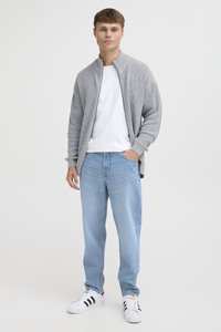 Cárdigan gris de cremallera con textura acanalada sobre una camiseta blanca, combinado con jeans azul claro y zapatillas blancas con franjas negras. Diseño minimalista.
