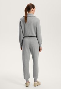 Gray knit jumpsuit with a high collar, elastic waistband, ribbed cuffs, and relaxed fit. Material appears soft with a smooth texture.