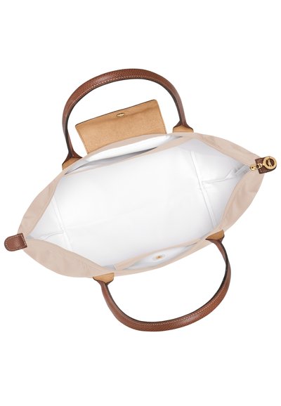 Beige tote bag with brown textured leather handles, featuring a spacious white interior and a small tan pocket with a gold closure.