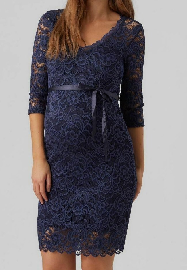 Femme portant une robe en dentelle florale bleu marine avec des manches trois-quarts et un ruban en satin noué à la taille.