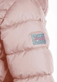 Artimas rožinės paminkštintos striukės rankovės vaizdas su mažu blizgiu stačiakampiu logotipo etikete, kurioje yra užrašas "Minoti".