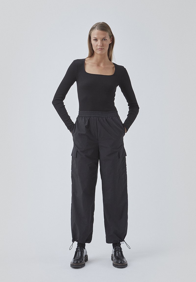 Sort langærmet fitted top med firkantet halsudskæring, parret med løse sorte cargo bukser med sidelommer og elastisk talje. Sorte støvler.