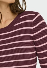 Pull en maille côtelée avec un motif rayé bordeaux et rose pâle, col rond et coupe ajustée. Texture douce avec un léger stretch.