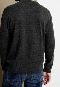 Tmavě šedý pletený svetr s kulatým výstřihem, žebrovanými manžetami a lemem. Nošený s modrými džínami, které zdůrazňují texturovanou tkaninu.