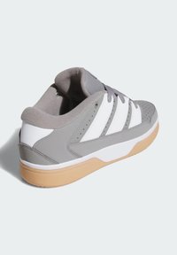 Šedá športová obuv s bielymi pruhmi, gumovou podrážkou, perforovanou špičkou, mäkkým vrchným materiálom a polstrovaným golierom.
