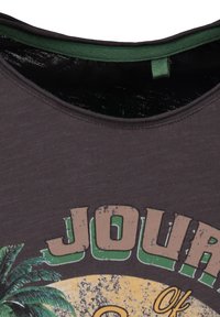Camiseta de color gris oscuro con cuello redondo, con un cuello interior verde, que presenta una impresión gráfica de palmeras y la palabra "JOURNEY" en beige y verde.