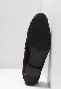 Chaussure en daim marron foncé avec une semelle en caoutchouc plate. L'empeigne présente une texture lisse et de subtils détails de couture le long du bord.