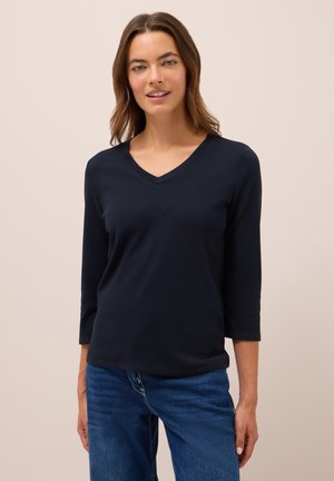 Mörkblå, lätt, långärmad V-hals t-shirt med en slät yta. Matchas med denimjeans, synlig sömnad vid plaggkanterna.