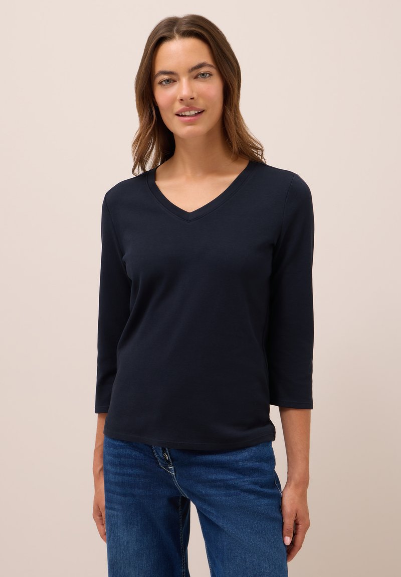 Marineblaues, leichtes, langärmliges V-Ausschnitt-Shirt mit glatter Textur. Kombiniert mit Jeans, sichtbare Nähte an den Kanten des Kleidungsstücks.