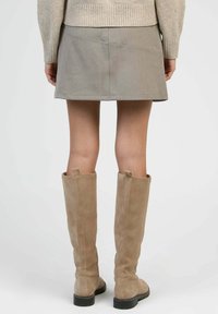 Jupe mini grise au design simple, en tissu texturé et taille mi-haute, associée à des bottes beige en daim jusqu'aux genoux avec une semelle plate.