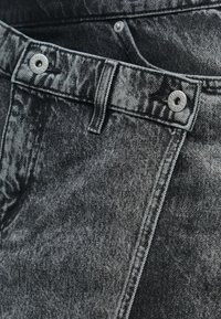 Fekete farmernadrág fakó textúrával, ezüst színű fém kiegészítőkkel és látható varrással. Gombos záródással és övbújtatókkal rendelkezik.