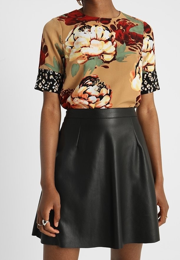 Top beige con patrón floral y acentos en las mangas negros, combinado con una falda plisada de piel sintética negra. Tejido texturizado y silueta ajustada.