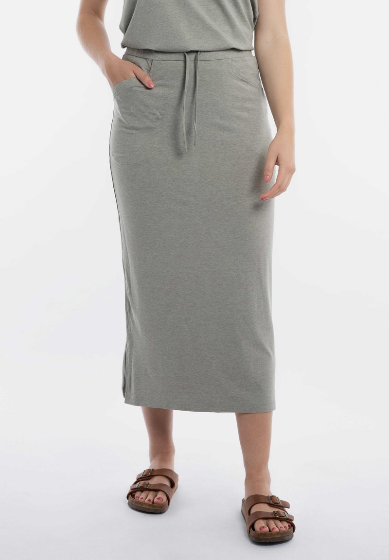 Grijze jersey rok tot de knie met een trekkoord in de taille, zijzakken en splitten aan de onderkant. Gepaard met bruine sandalen.