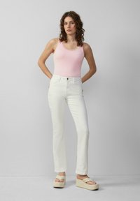 Witte rechte spijkerbroek met hoge taille, gecombineerd met een roze geribbelde tanktop met kantafwerking. Model draagt beige platform sandalen.