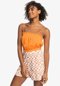 Orange, elastisk talje top med tynde stropper; parret med hvide shorts med et orange ternet og blomstermønster. Tekstureret stof.