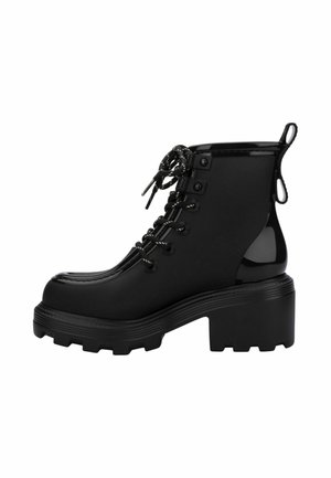Bottine noire à plateforme épaisse, avec lacets sur le devant, bout arrondi et languettes à tirer sur le talon et la languette, vue de côté.