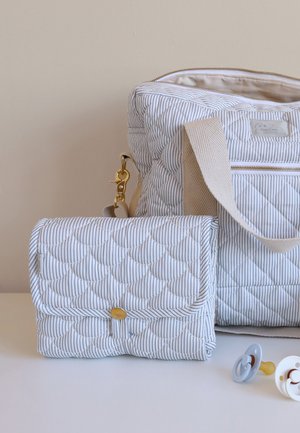 Geantă pentru scutece matlasată cu dungi, cu curea bej, saltea pliabilă asortată pentru schimbat scutece și două suzete pentru bebeluși, pe o suprafață albă.