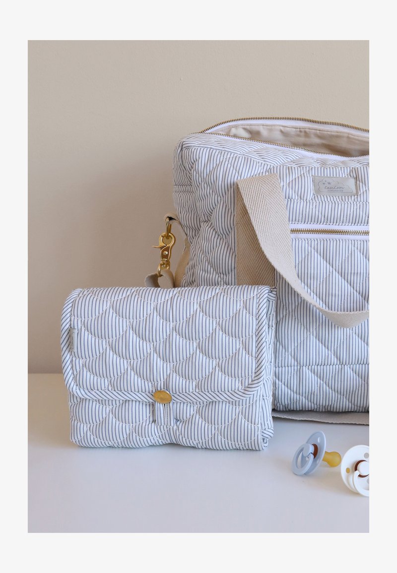 Sac à langer matelassé rayé avec sangle beige, matelas à langer pliable assorti, et deux sucettes pour bébé sur une surface blanche.