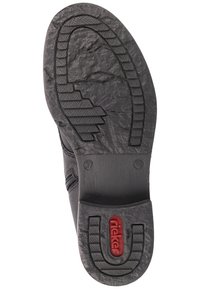 Semelle de chaussure en caoutchouc noir avec des motifs de grip texturés, présentant un logo rouge bien visible et une indication de taille, des sections lisses et une forme profilée.