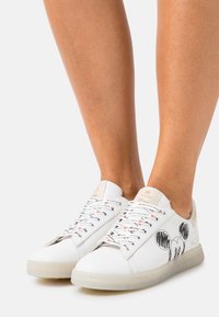 White sneakers with a smooth leather finish, featuring a large Mickey Mouse graphic and script detail on the sides. Transparent rubber sole.