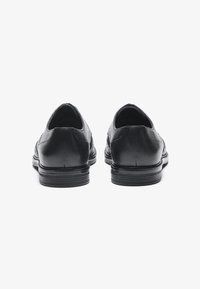 Chaussures en cuir noir avec une texture lisse, bout rond et un petit talon empilé. Pas de matériel visible ni de motifs distincts.