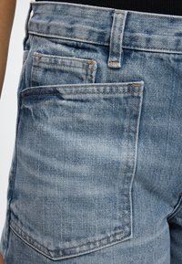 Κοντινό πλάνο ενός ατόμου που φοράει ανοιχτό μπλε τζιν με διπλές πίσω τσέπες και ορατές ραφές στις θηλιές της ζώνης.