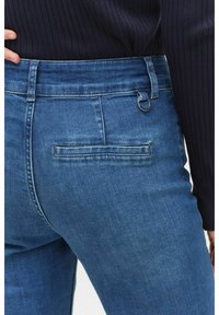 Mörkblå denimjeans med en figursydd design, medelhög midja och en bakficka med horisontell sömdetalj. Inkluderar en metallöga som accent.