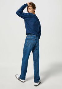Dżinsy w ciemnoniebieskim kolorze, o prostym kroju z widocznymi szwami. Połączone z granatową koszulą z długim rękawem i białymi trampkami.