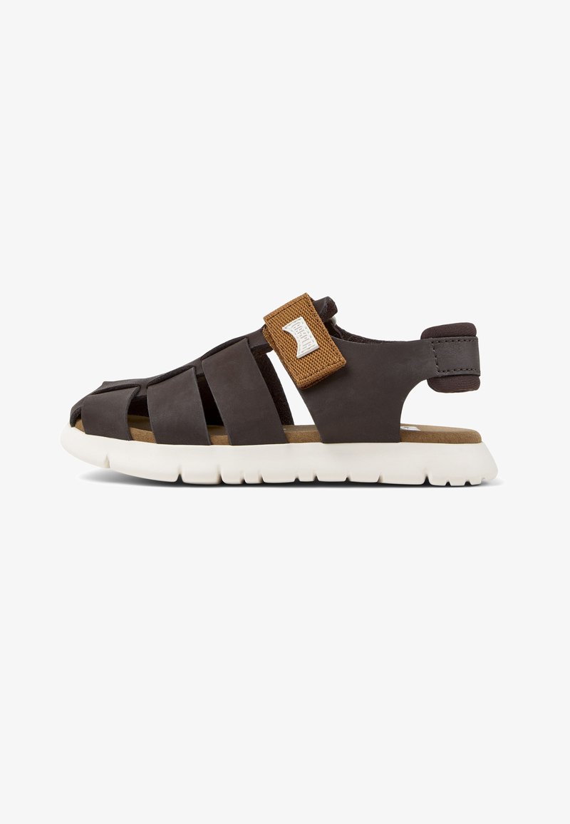 Sandale en cuir marron avec un design ajouré, semelle blanche et bride marron ajustable. Semelle intérieure douce avec un intérieur texturé beige.