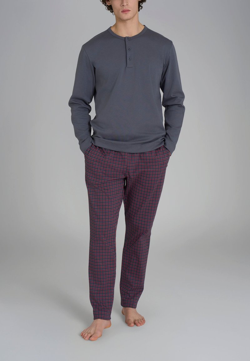 Maglia grigia a maniche lunghe con scollo henley e tre bottoni, abbinata a pantaloni a quadri rossi e blu in un tessuto morbido.