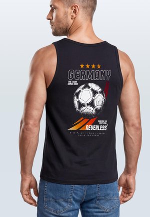Mann trägt schwarzes ärmelloses Hemd mit Design der deutschen Fußballnationalmannschaft und Text auf dem Rücken, kombiniert mit blauen Jeans.
