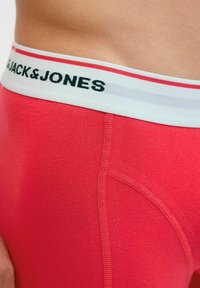 Rote Baumwoll-Boxershorts mit einem weißen elastischen Bund, der mit schwarzem "JACK&JONES"-Schriftzug versehen ist. Glatte Textur und verstärkte Nähte.