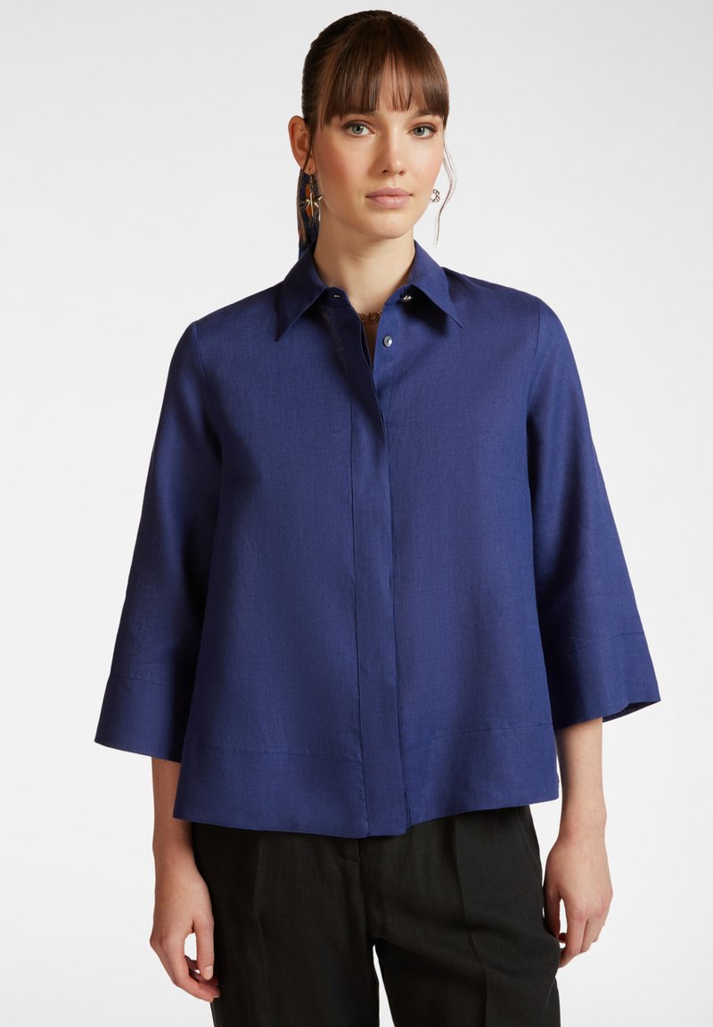 Camicia blu navy con colletto, maniche a tre quarti e chiusura frontale con bottoni. Tessuto liscio con una sottile trama.