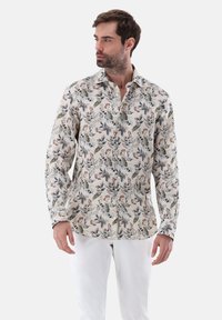 Camicia a maniche lunghe in tessuto leggero color crema con una stampa floreale e di foglie in tonalità di blu, verde e ruggine; presenta una chiusura con bottoni e colletto.