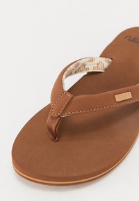 Brown flip-flop with textured upper strap, flat cushioned footbed, and light-colored outsole. Features logo detail on strap.