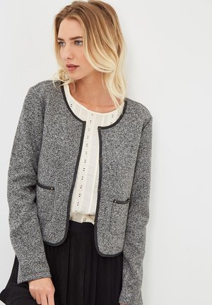 Chaqueta gris texturizada con cuello redondo, ribete negro, dos bolsillos delanteros y cierre de botones, llevada sobre una blusa clara con pliegues.