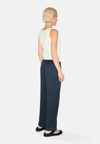 White ribbed tank top, navy wide-leg trousers with subtle texture, and black sandals, viewed from the back.