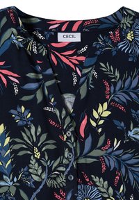 Blouse bleu marine foncé avec imprimé floral coloré en vert, rose, bleu et jaune, avec un col sans col et trois boutons noirs sur le devant.