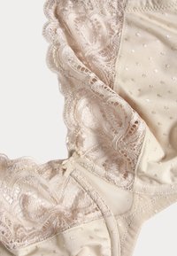 Beige lingerie met kantafwerking en een stippenpatroon. Bevat ingewikkelde kantdetails en een kleine strikaccent aan de zijkant.