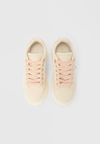 Bež superge z gladkim sintetičnim zgornjim delom, roza poudarki, okrogel prst in teksturirane vezalke. Na peti je logotip in oblazinjen rob.