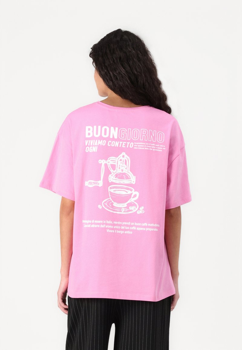 Rosa, oversized t-skjorte laget av bomull med et hvitt kaffe-tema grafikk og tekst på baksiden, med ledige kort ermer.