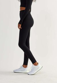 Black high-waisted leggings with a textured finish, paired with white athletic shoes featuring a mesh upper and three-stripe design.