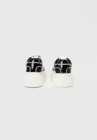 Μαύρα παπούτσια sneakers από πατενταρισμένο δέρμα με χοντρή λευκή ριμπ σόλα. Περιλαμβάνει branding στη φτέρνα και δέσιμο με κορδόνια μπροστά.