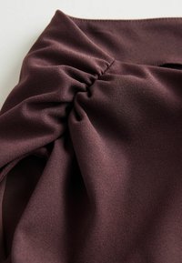 Tissu violet foncé avec un détail froncé créant des plis texturés et des ombres douces sur une surface lisse.