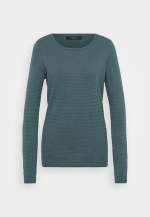 Teal spalvos ilgas rankovės megztinis, pagamintas iš tekstūruotos medžiagos, su apvalia iškirpte ir su raukšlėmis. Yra geometrinis raštas.