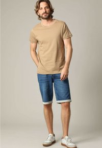 Beige katoenen t-shirt met korte mouwen en geborduurde details, gecombineerd met opgerolde denim shorts en witte sneakers met bruine zolen.