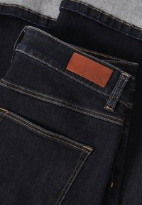 Tmavomodré riflové nohavice s oranžovým prešitím a hnedou koženou nášivkou. Majú klasický dizajn s 5 vreckami a hladkú textúru.