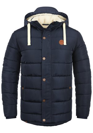 Veste matelassée bleu marine avec capuche, accents crème, boutons-pression, et doublure intérieure en polaire. Design rembourré avec poches latérales.